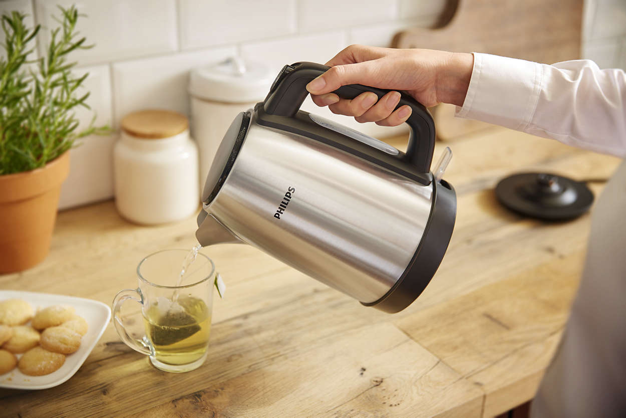 Person pouring tea into a glass, on a wooden countertop. Kettle and cookies visible.