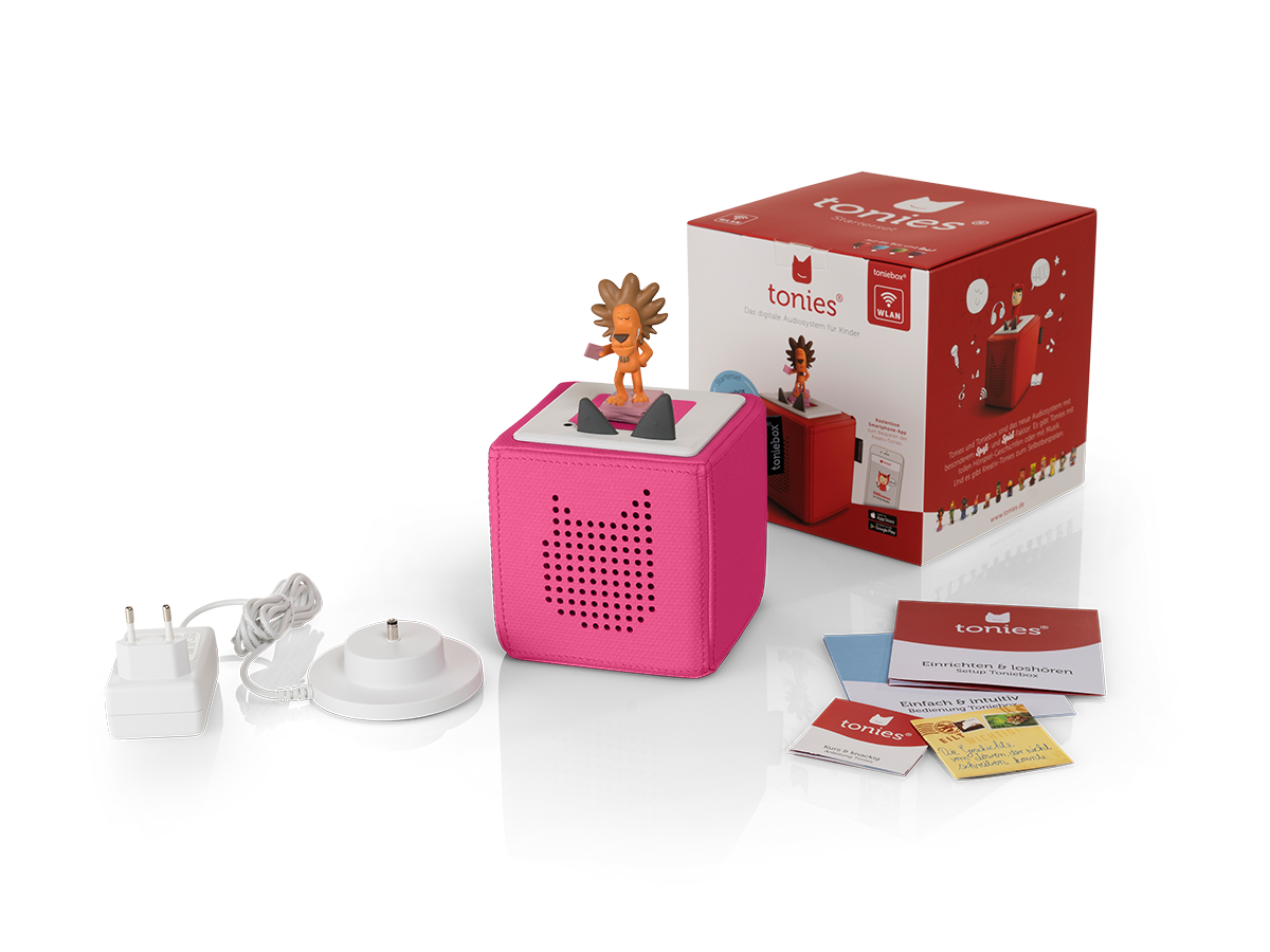 Eine pinke Toniebox mit Löwenfigur, Box, Karten, Ladegerät und Basis, alles auf schwarzem Hintergrund.