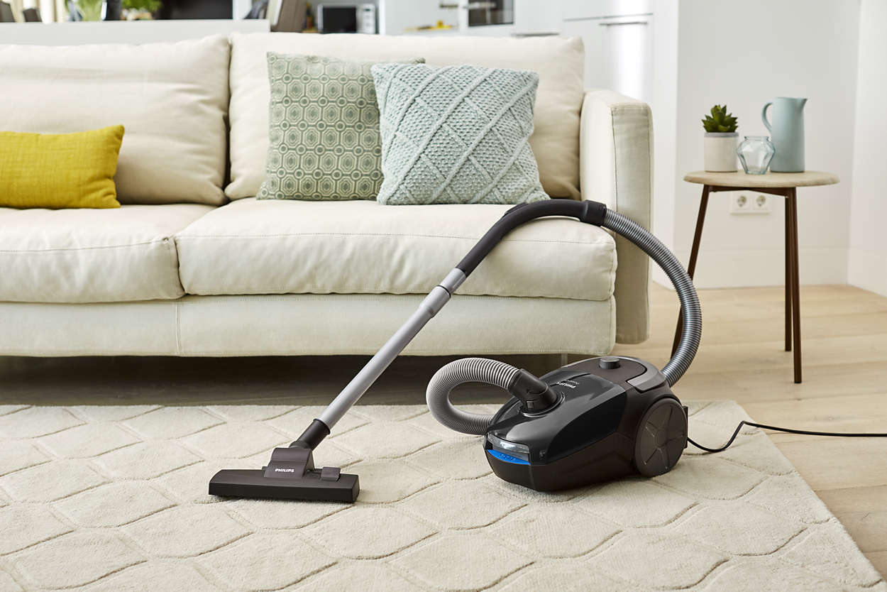 A vacuum cleaner on a patterned rug in a living room with a couch and a side table.