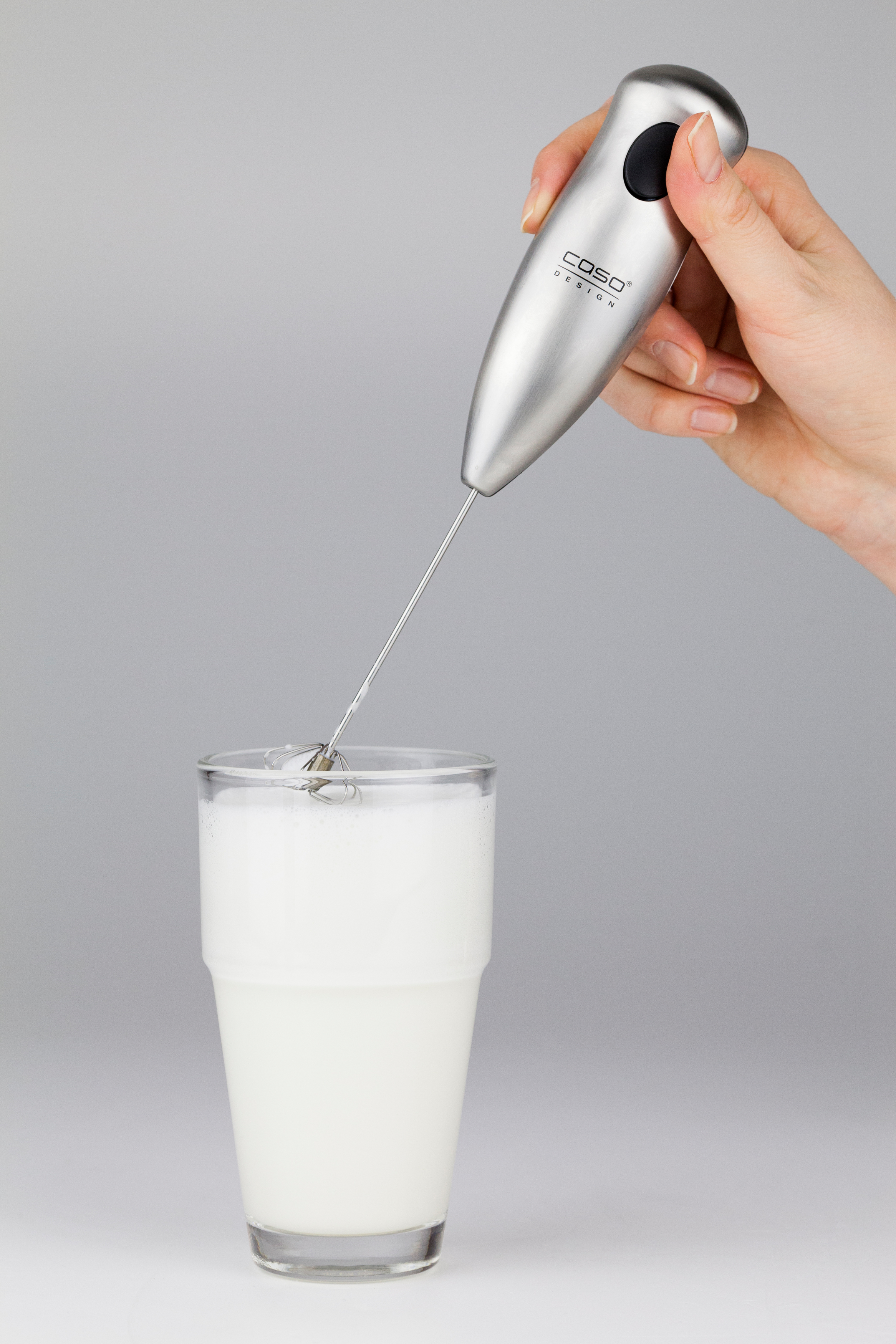 Eine Hand, die einen Milchaufschäumer über einem Glas Milch hält. Schaum bildet sich.