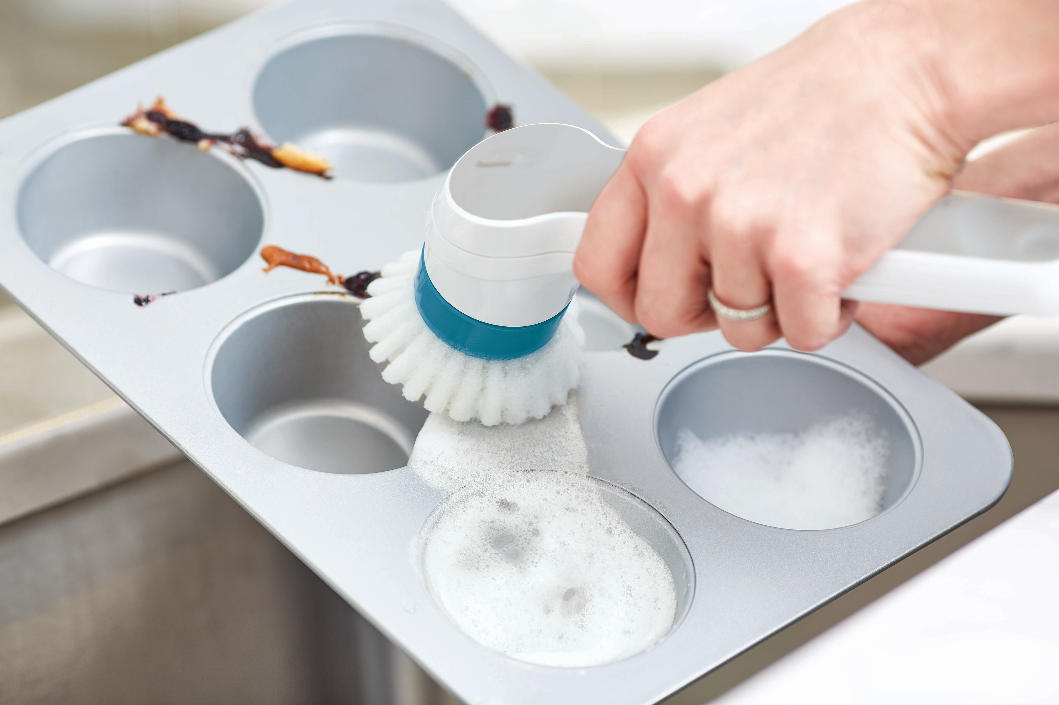 Person reinigt eine Muffinform mit einer elektrischen Bürste und Seifenwasser.