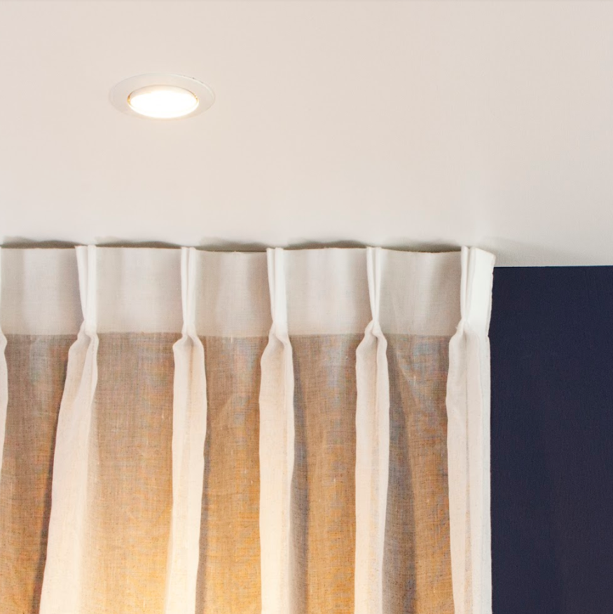 White ceiling with a recessed light, white curtains and a dark blue wall.