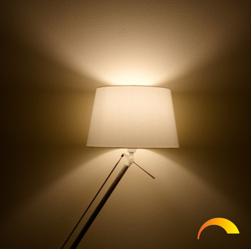 A lamp with a white shade illuminates the wall. Light radiates from the lamp.