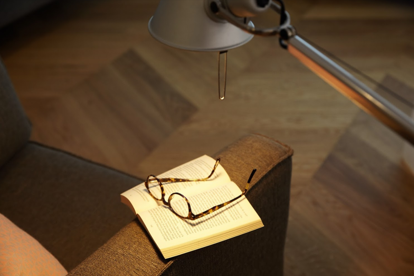 Open boek met bril, een lamp schijnt. Het boek ligt op een bruine bank.