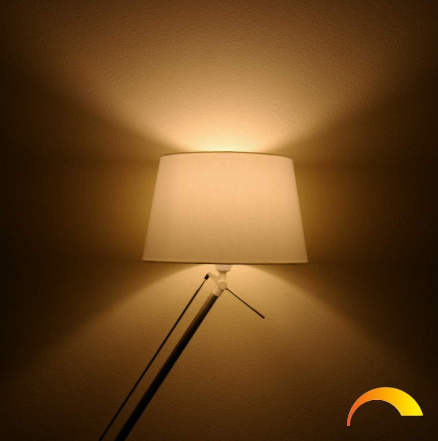 Een staande lamp werpt warm licht op een beige muur, met een zonnesymbool.