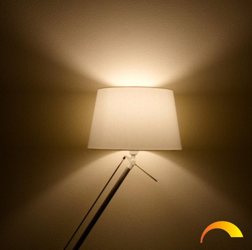 Een witte lampenkap op een lamp, die licht op de muur werpt. Een warme oranje gloed is zichtbaar.