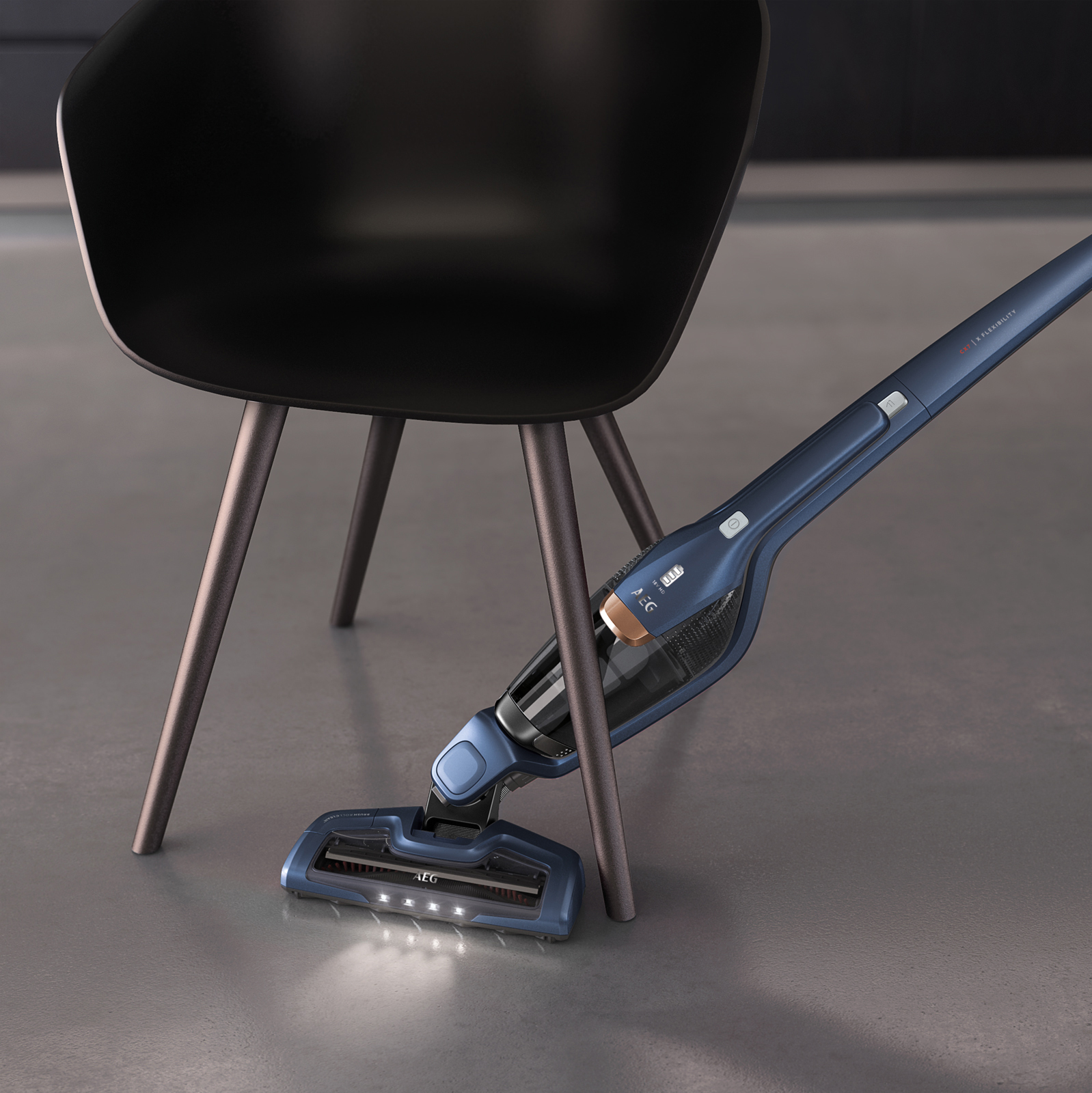 Ein blauer kabelloser Staubsauger in der Nähe eines schwarzen Stuhls auf grauem Boden.