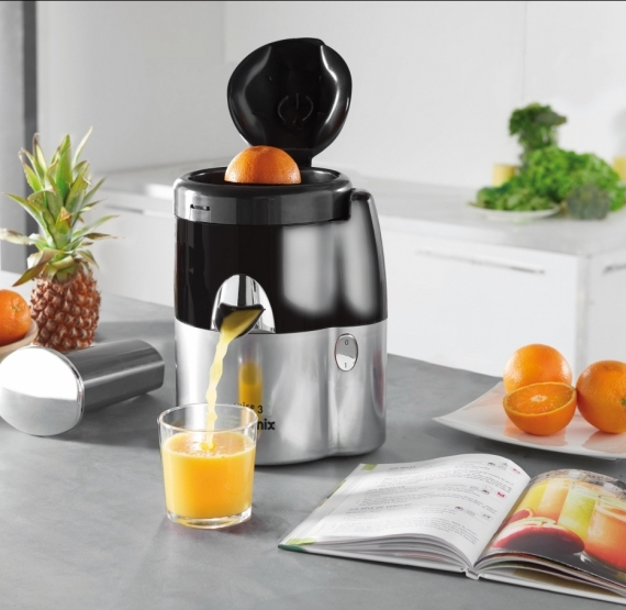 Extracteur de jus avec une orange à l'intérieur et du jus versé dans un verre. Oranges et ananas.
