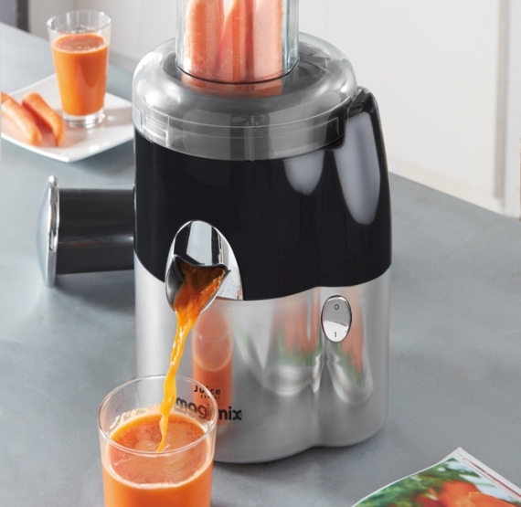 Extracteur de jus en action, jus versé dans un verre, carottes en haut et un verre de jus.