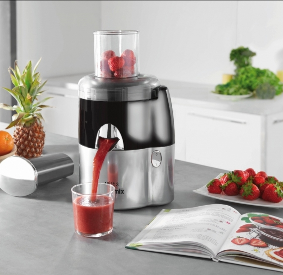 Extracteur de jus avec des fraises pressées dans un verre. Ananas et autres fruits visibles.