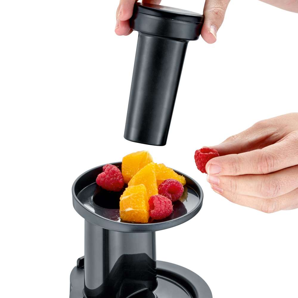 A person assembling a black juicer with fruits. Oranges and raspberries.