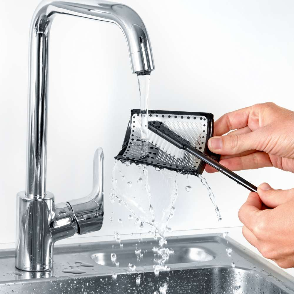 A person cleaning a black filter with a brush under running water at a sink.  The brush is black.