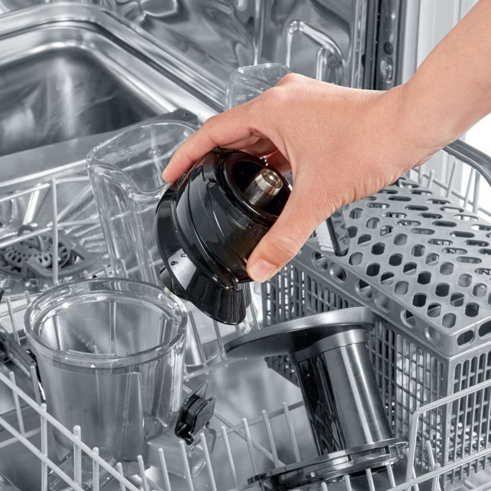 A hand places a black object into a dishwasher rack with other clear objects.