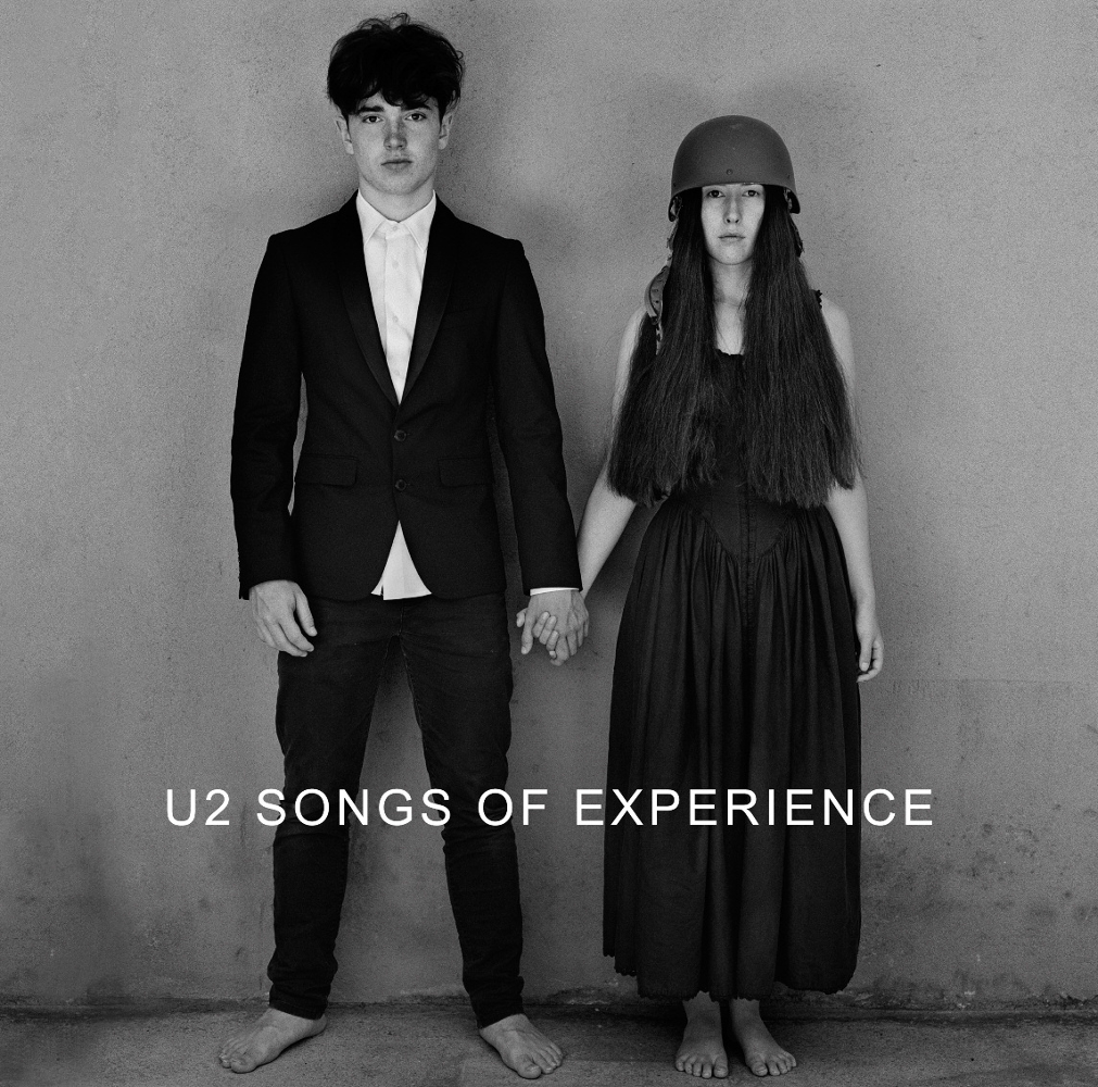 Fekete-fehér fotó. Két ember kézen fogva. A szöveg az U2 Songs of Experience.
