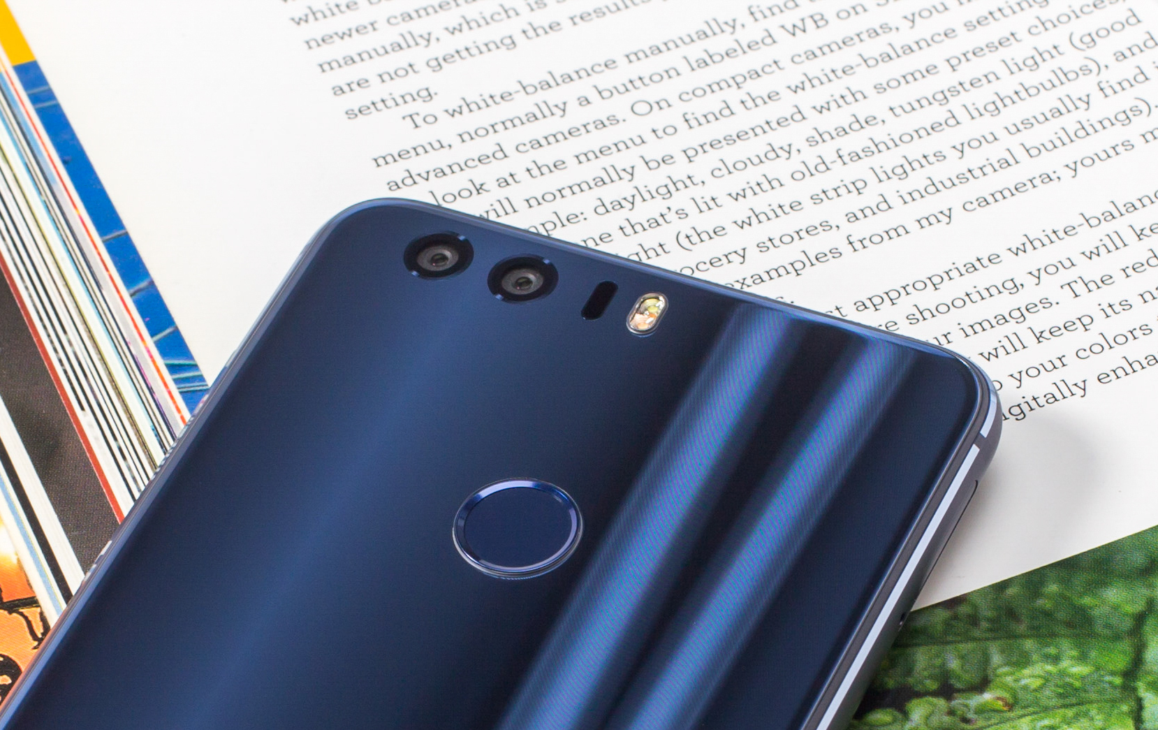 Ein blaues Telefon mit zwei Kameras und einem Fingerabdrucksensor auf einer Buchseite.