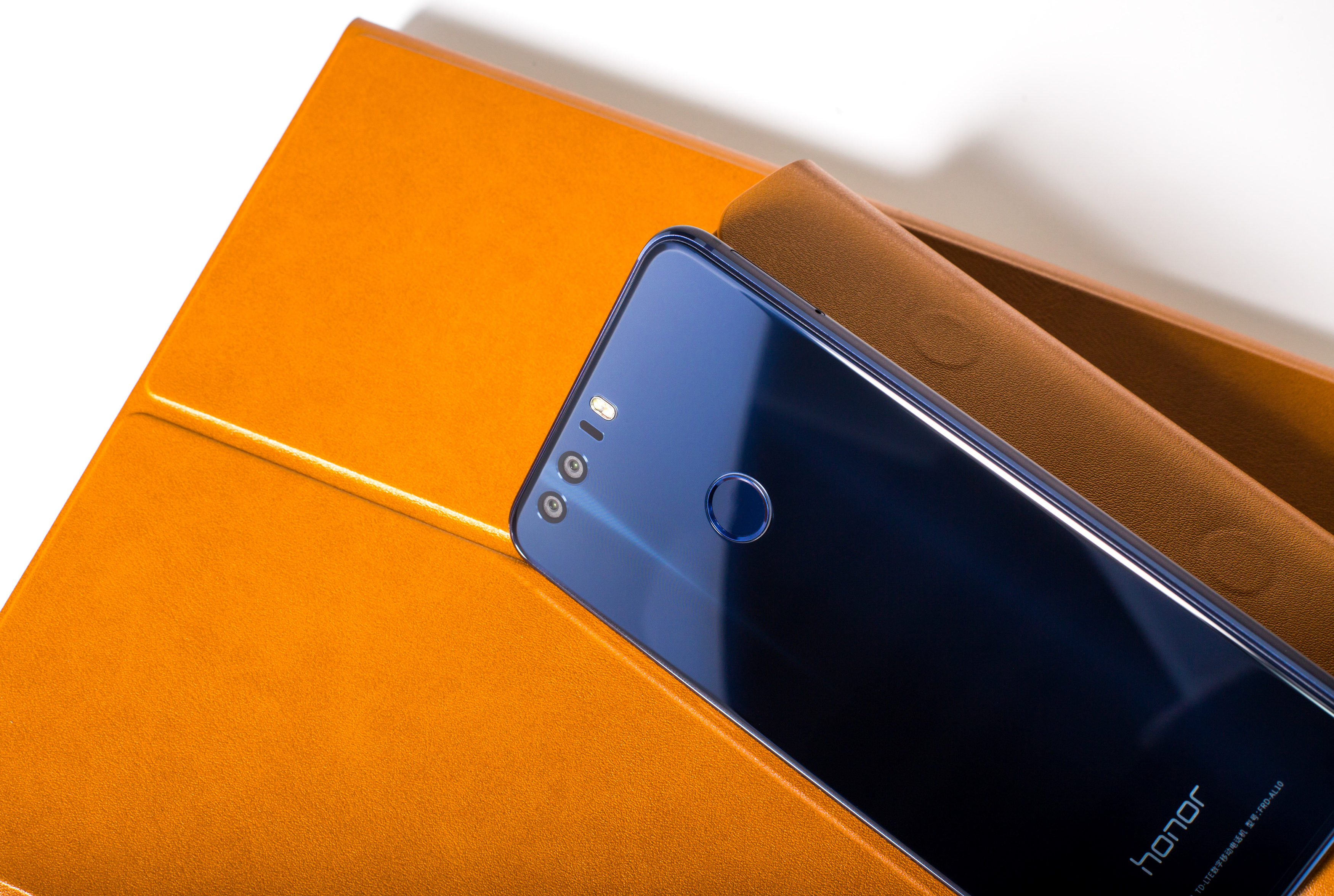 Blaues Smartphone auf orangefarbener Hülle. Braune Hülle sichtbar. Weißer Hintergrund.