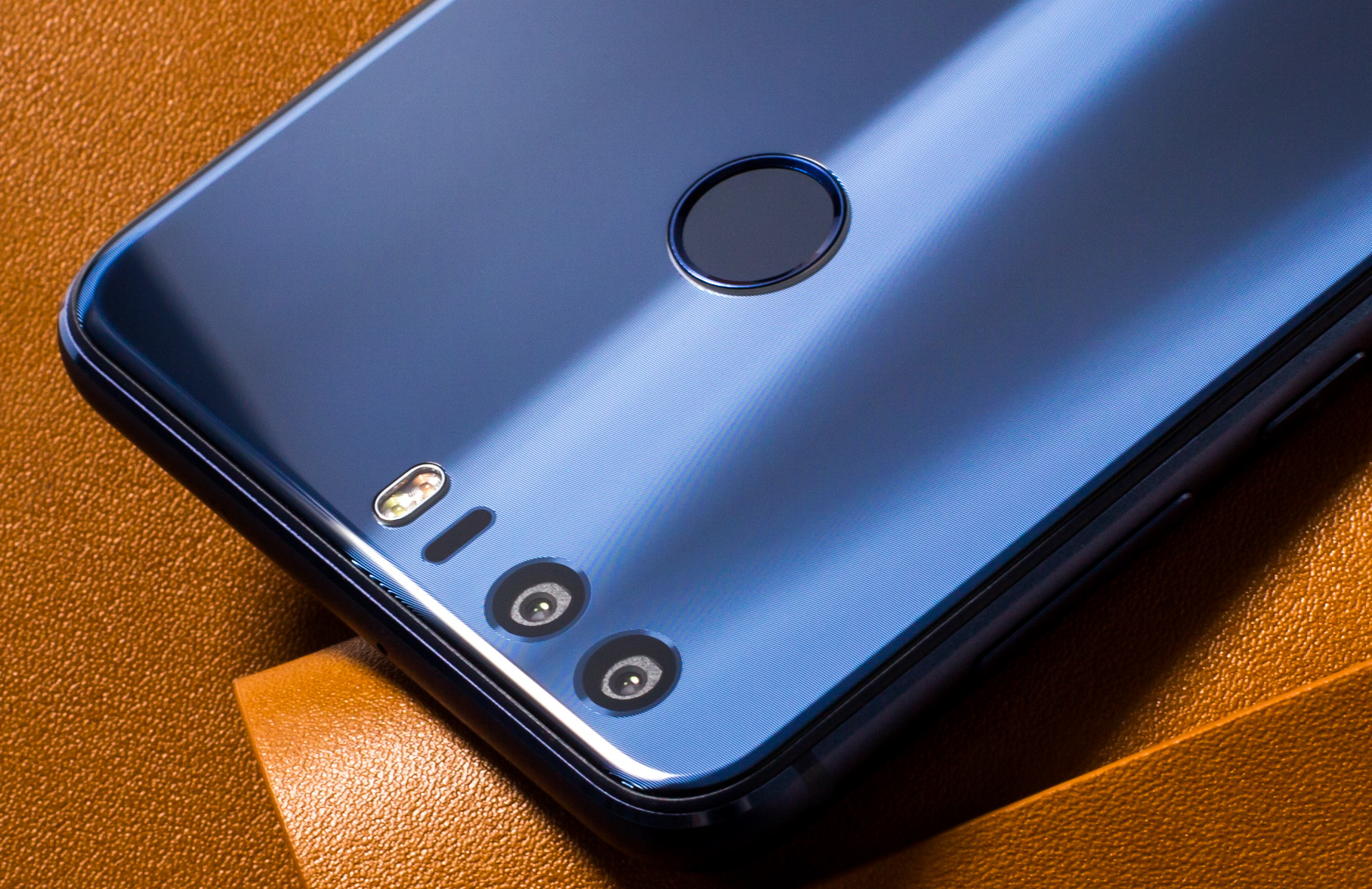 Nahaufnahme eines blauen Telefons mit drei Kameralinsen und einem Fingerabdrucksensor auf brauner Oberfläche.