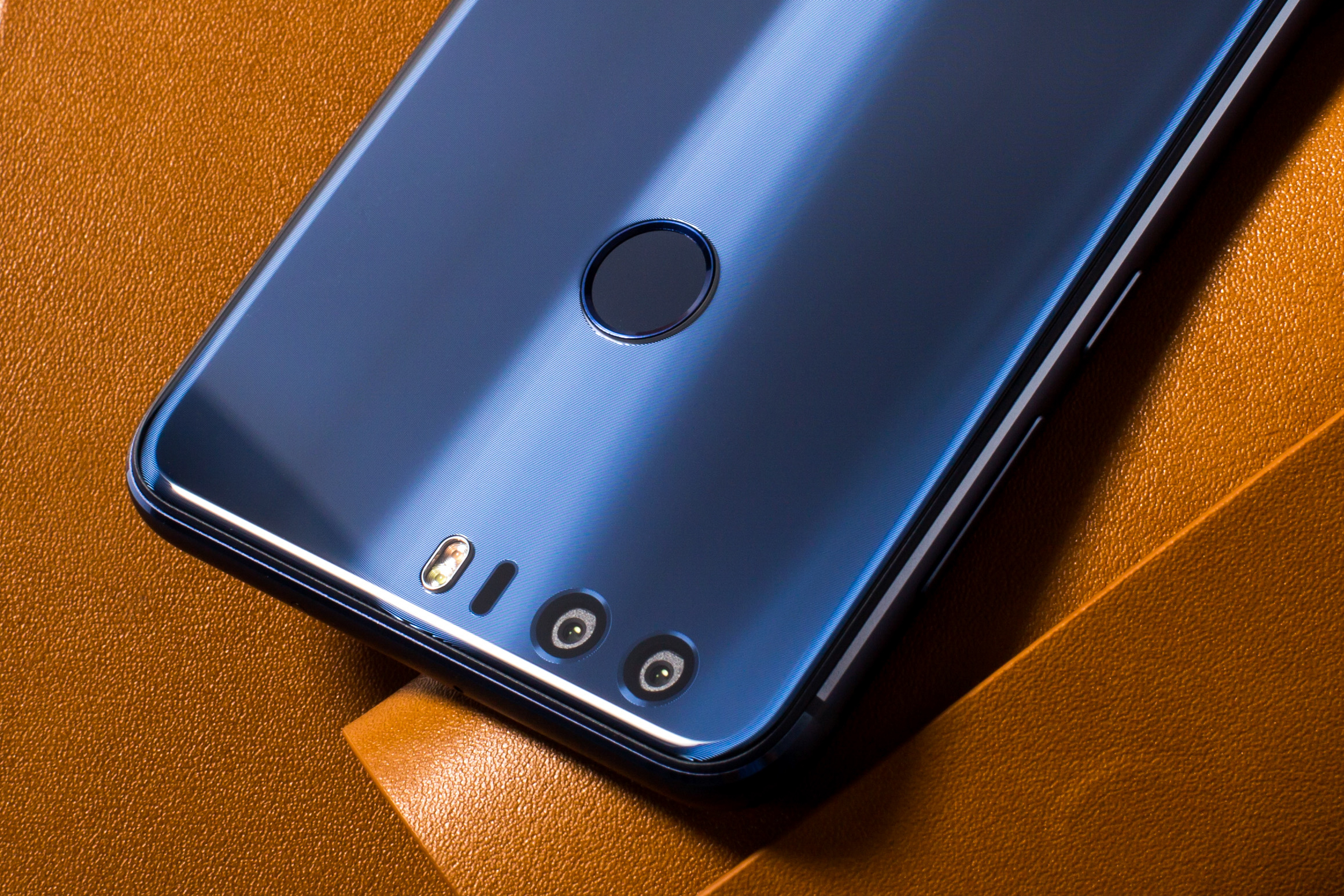 Nahaufnahme der Rückseite eines blauen Smartphones. Es hat eine Kamera und einen Fingerabdrucksensor auf brauner Oberfläche.