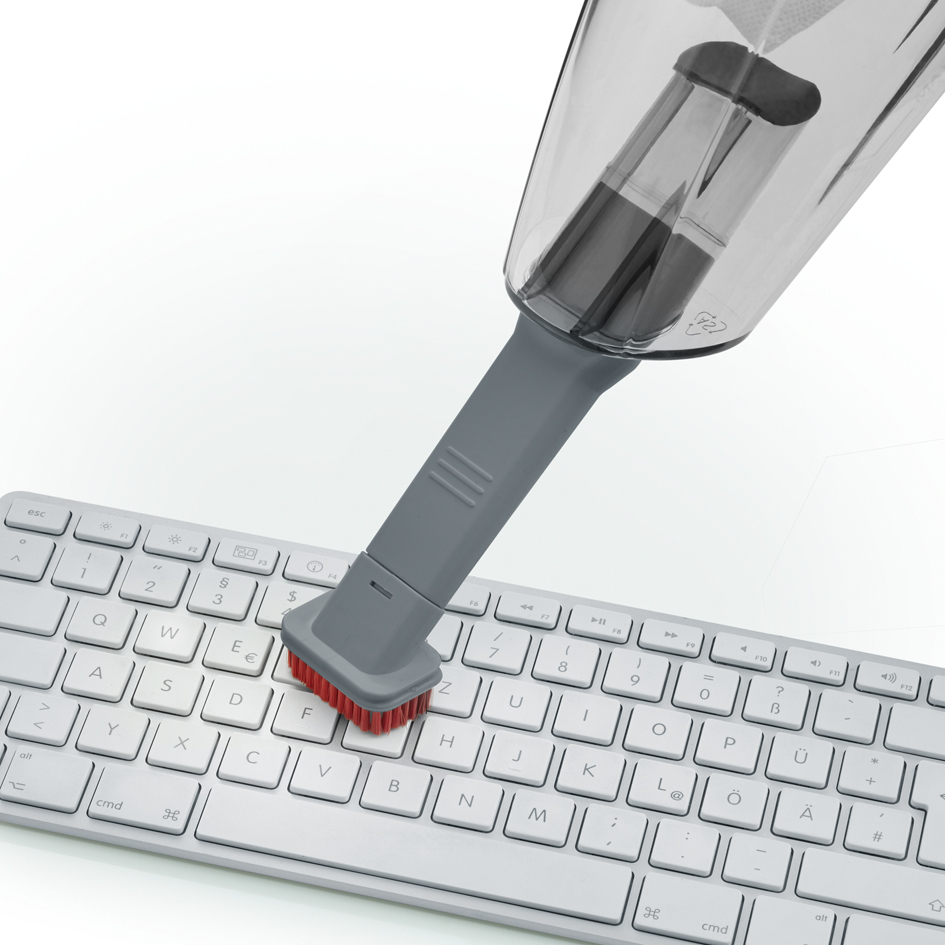 Aspirateur à main nettoyant un clavier. Le clavier est blanc, l'aspirateur gris.