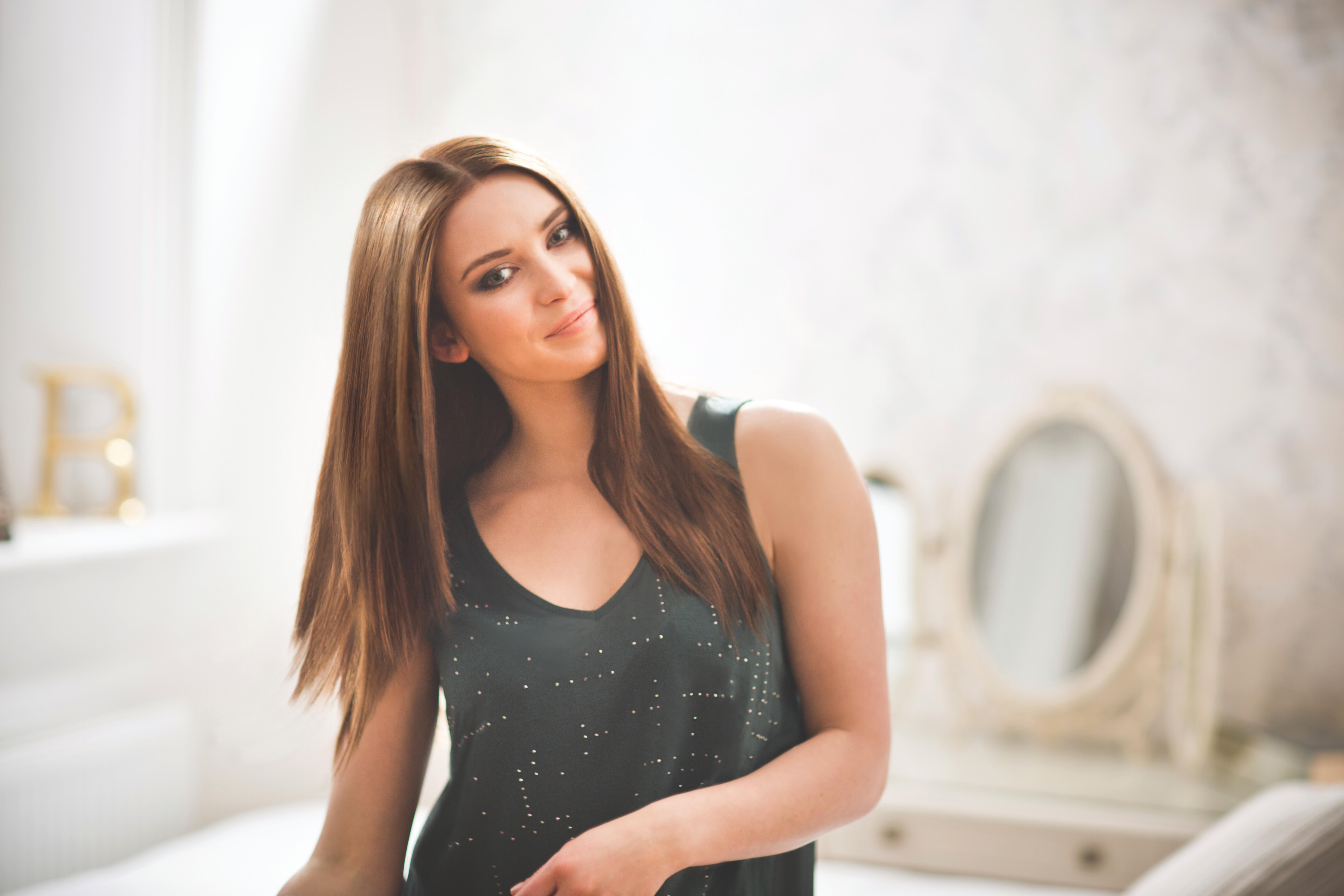 Woman in a sleeveless top, looking at the camera. Long brown hair, light background.
