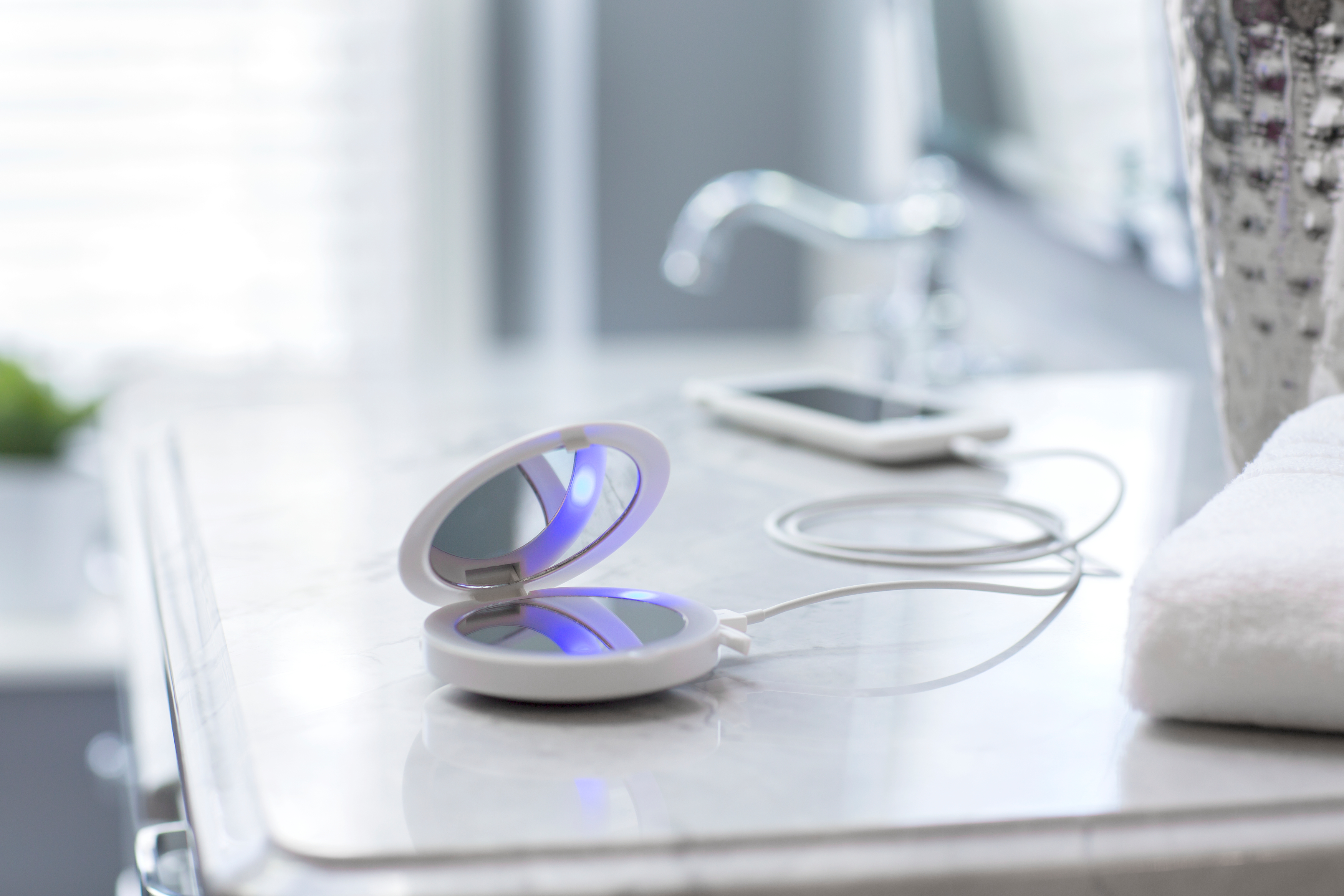 Spiegel mit Licht auf Marmortisch, Telefon und Wasserhahn im Hintergrund.