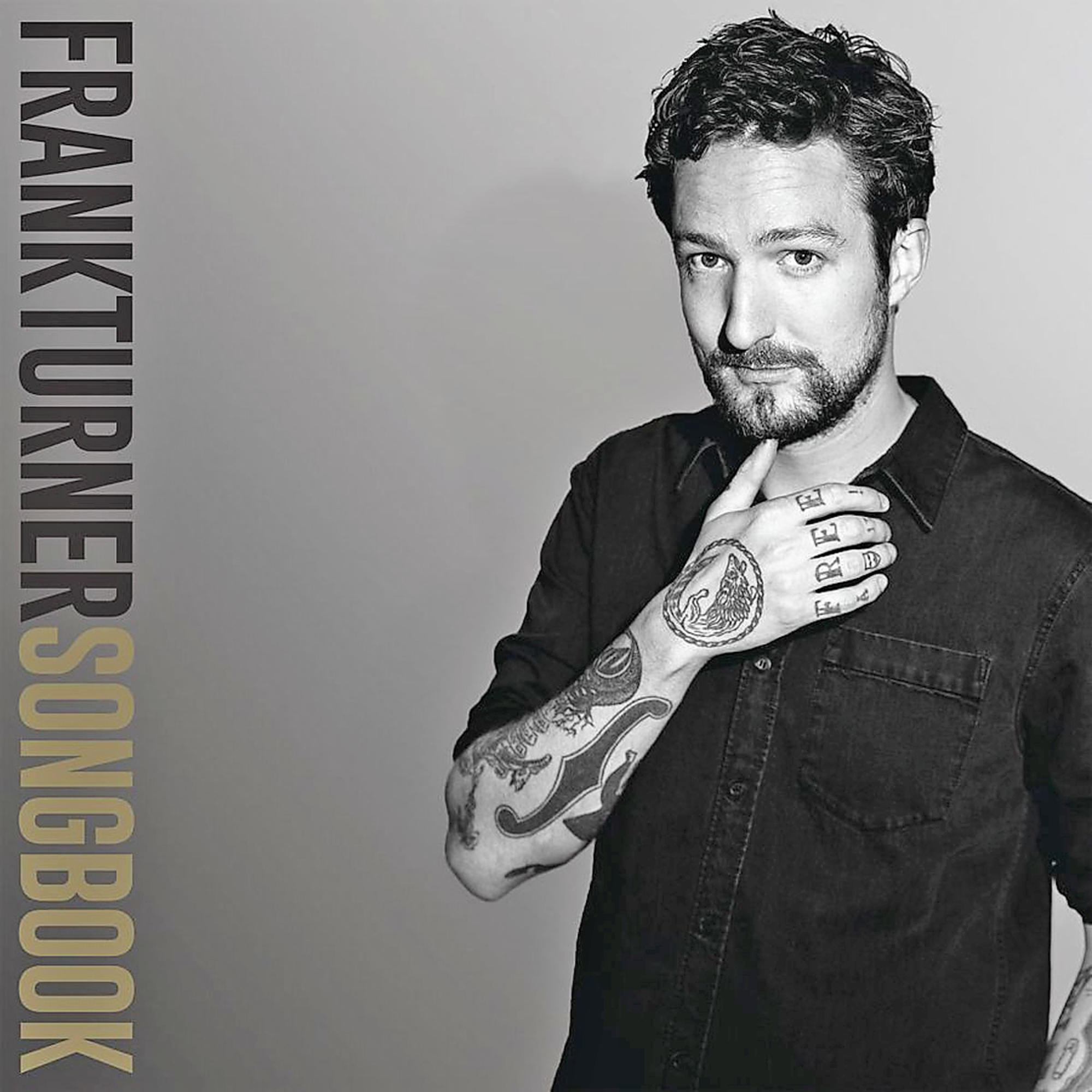 Een man met tatoeages op zijn arm en nek, die zijn kin vasthoudt. De titel 'FRANKTURNERSONGBOOK' staat op de zijkant.