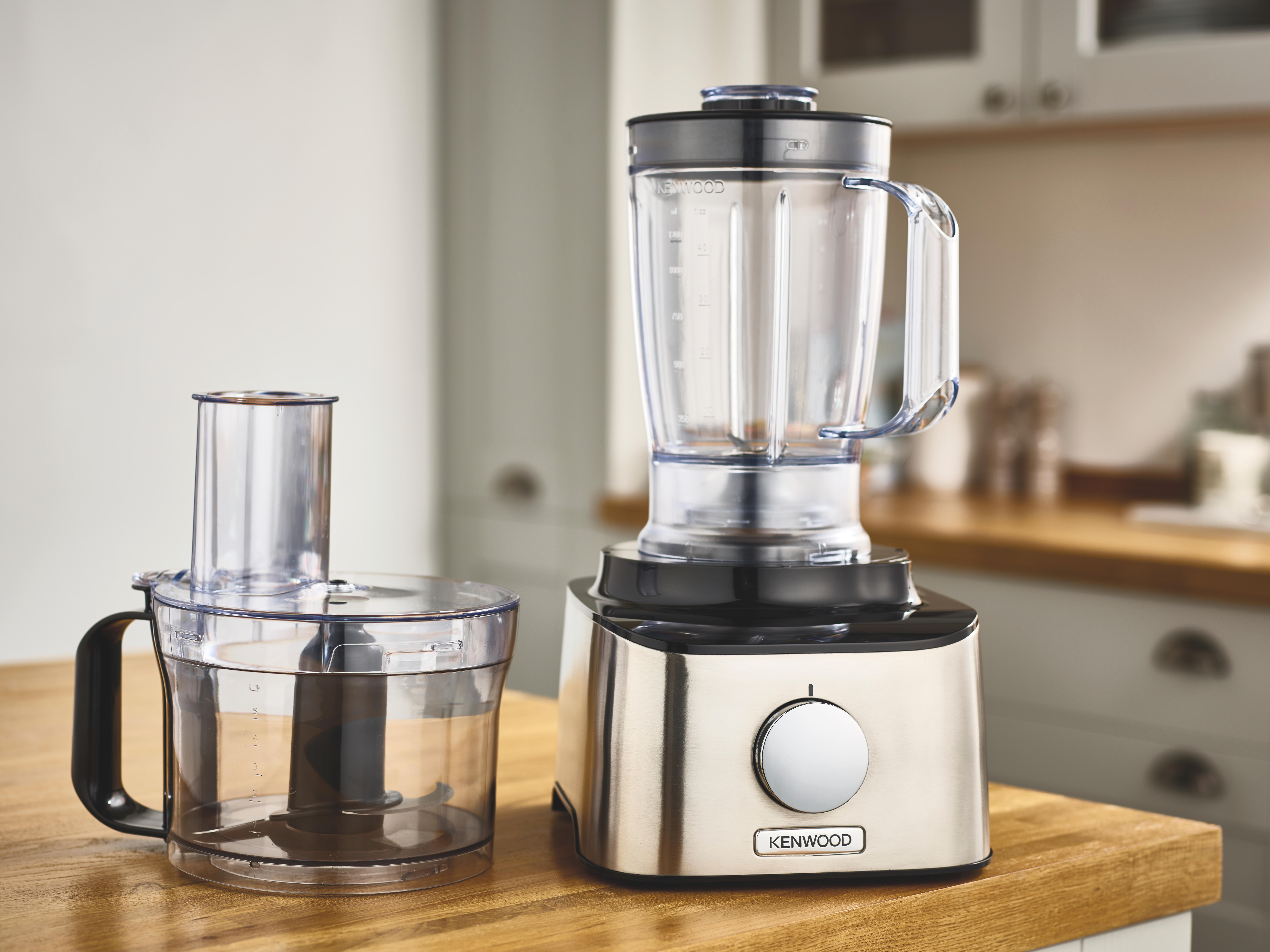 Twee keukenapparaten op een houten oppervlak. Eén is een blender, de andere een foodprocessor.