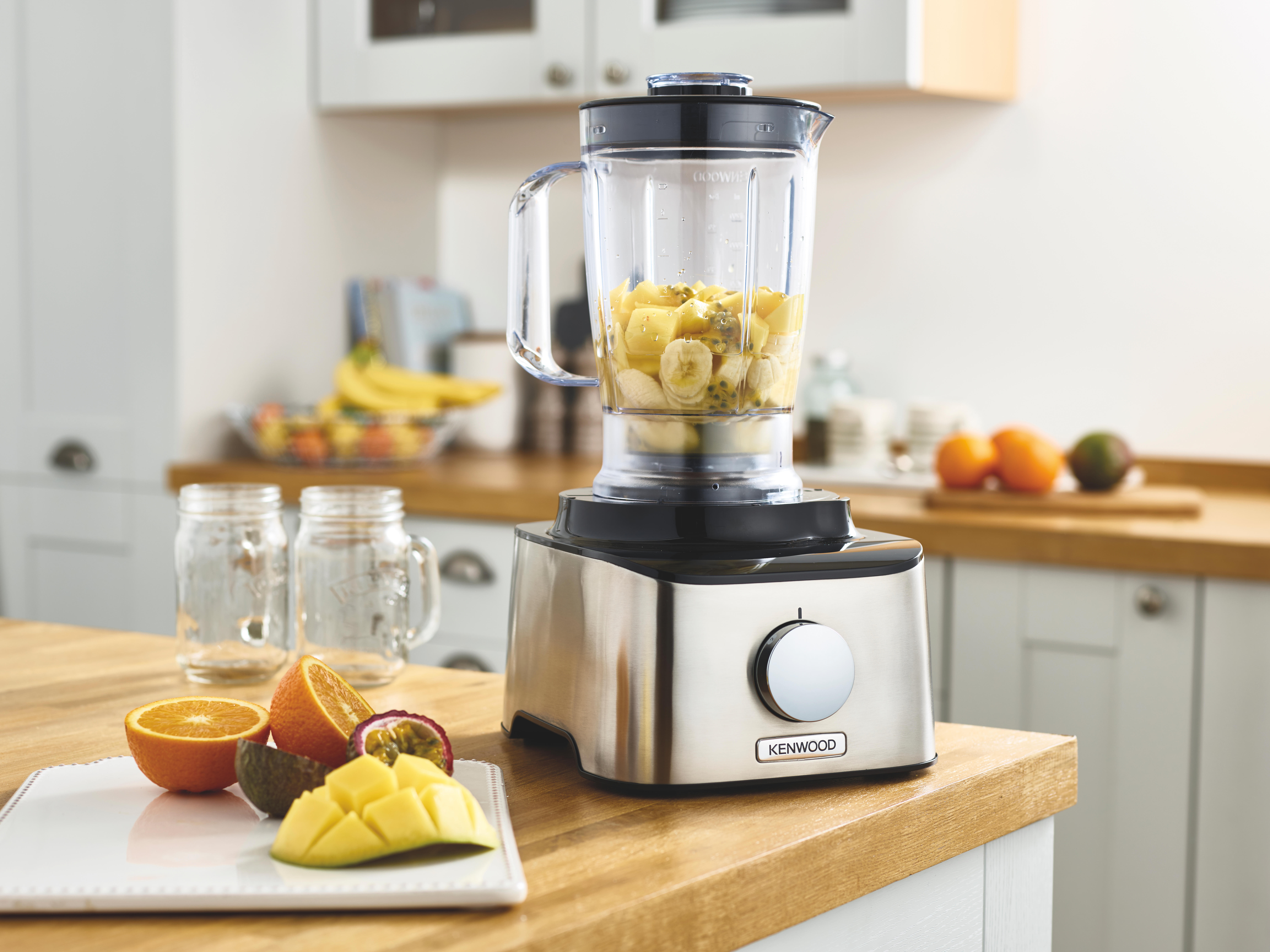 Blender op een houten aanrecht met gesneden fruit en weckpotten. Keuken op de achtergrond.