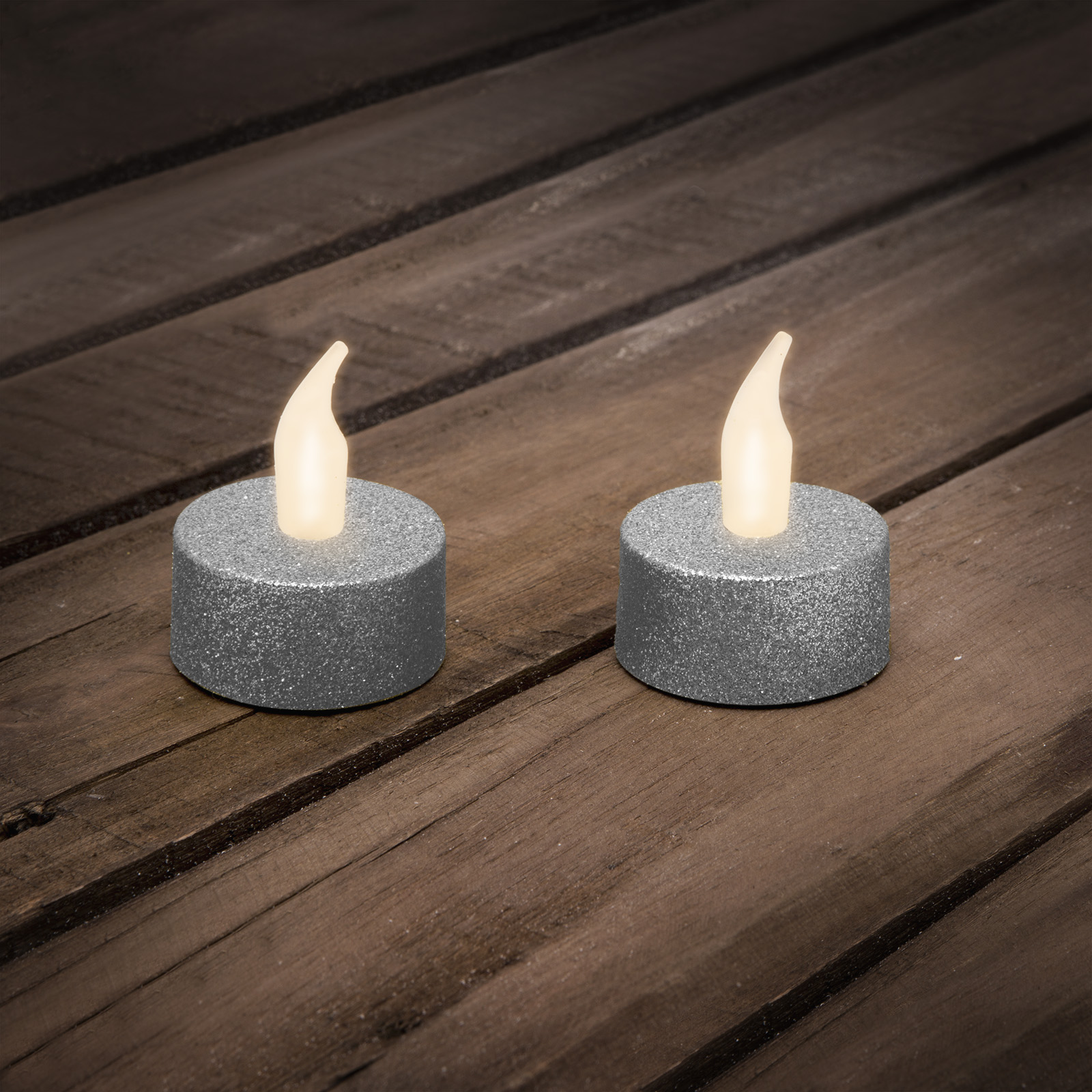 Két ezüst gyertya láng alakú fényekkel egy fa felületen.
