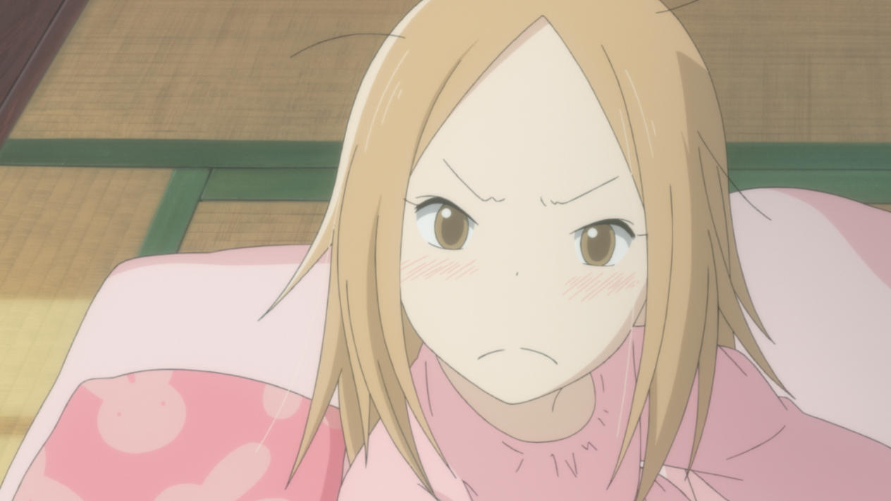 Ein Anime-Mädchen mit blonden Haaren und braunen Augen sieht verärgert aus. Sie trägt ein rosa Hemd und liegt auf einer rosa Decke.