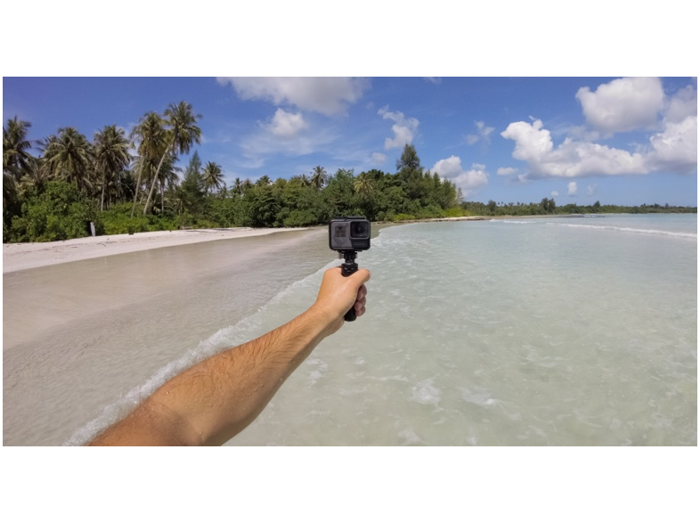 Személy GoPro kamerát tart tiszta vízben, háttérben a strand és az ég.