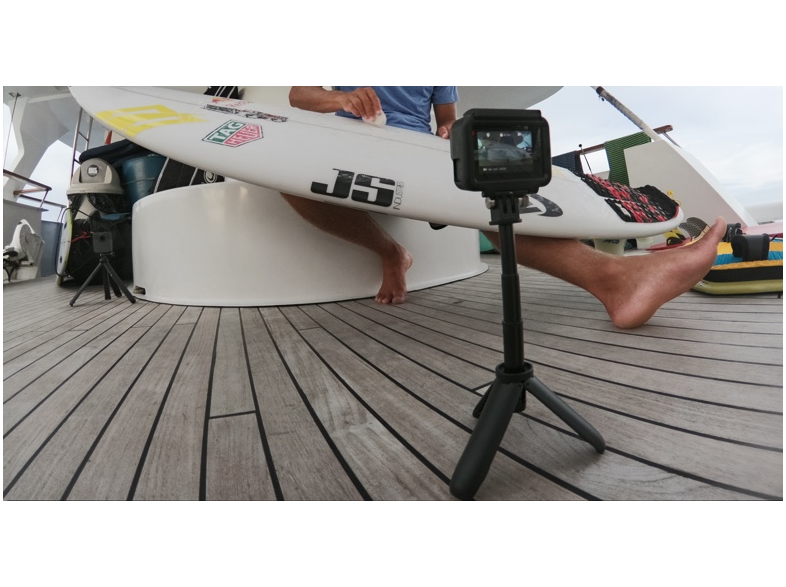 Személy egy hajón szörfdeszkával. GoPro kamera egy állványon elöl. Fa fedélzet.