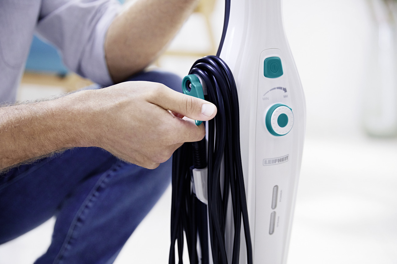 Eine Person, die ein Dampfreinigerkabel hält, mit einem Dampfreiniger im Hintergrund.