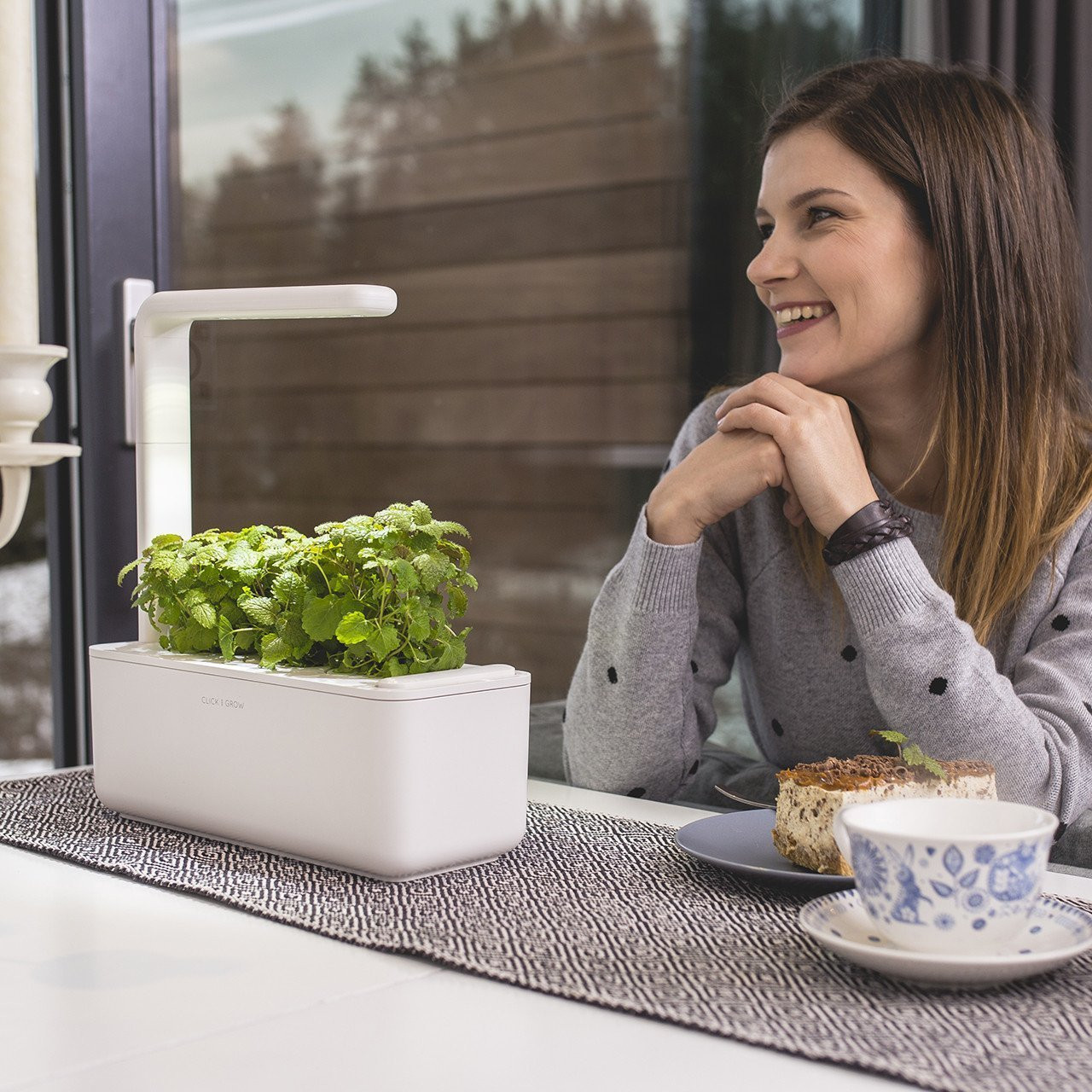 Een vrouw glimlacht terwijl ze naar een kleine binnentuin met planten kijkt. Een tafelsetting.