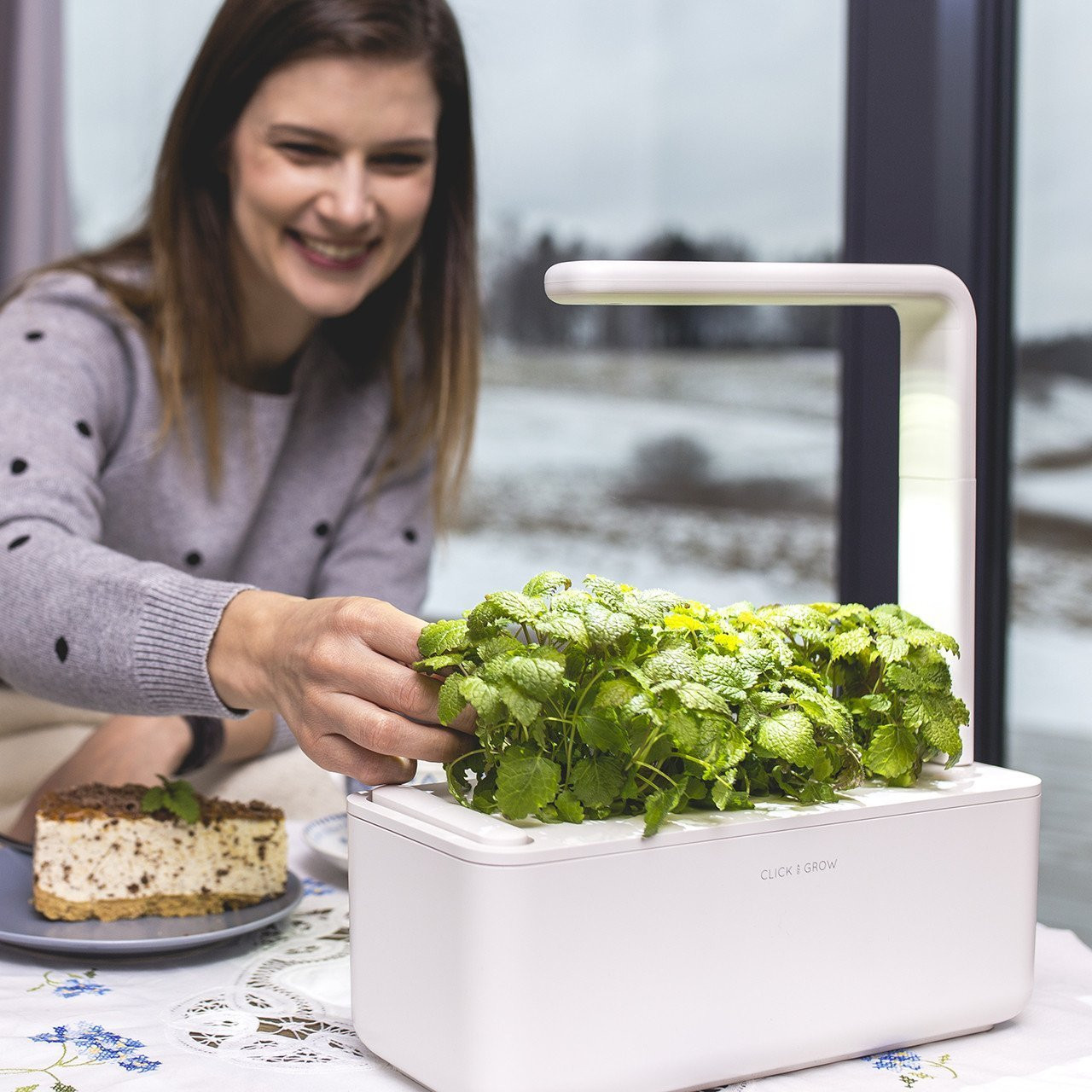 Vrouw die een kleine binnentuin met groene kruiden verzorgt, lachend.