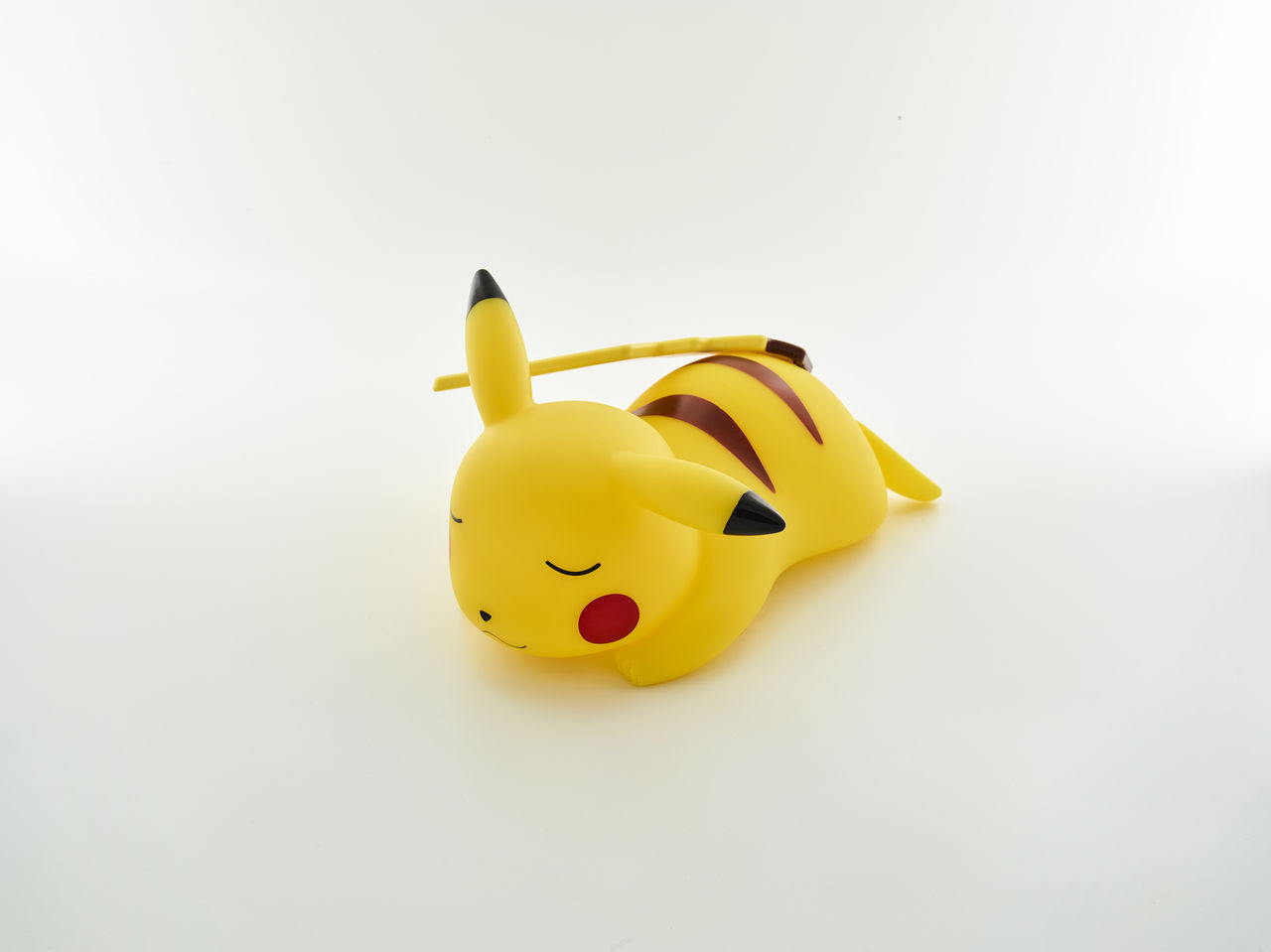 Gelbe Pikachu-Figur, die liegt, Augen geschlossen, mit roten Wangen, auf weißer Oberfläche.