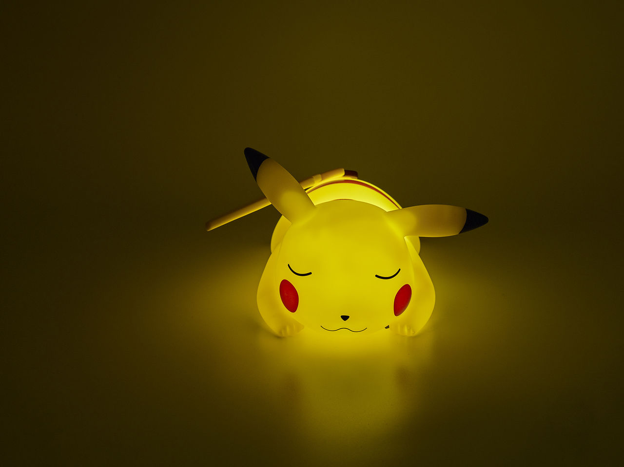 Ein gelbes Pikachu-Nachtlicht, das mit geschlossenen Augen liegt und in einem dunkelgelben Raum leuchtet.