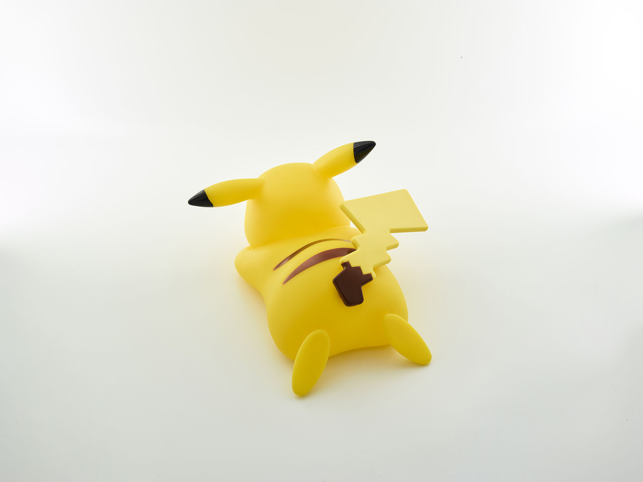Gelbe Pikachu-Spielfigur, Rückansicht. Weißer Hintergrund. Schwarze Streifen.