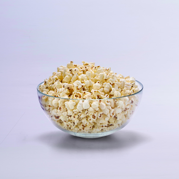 Een glazen kom vol popcorn op een witte achtergrond.