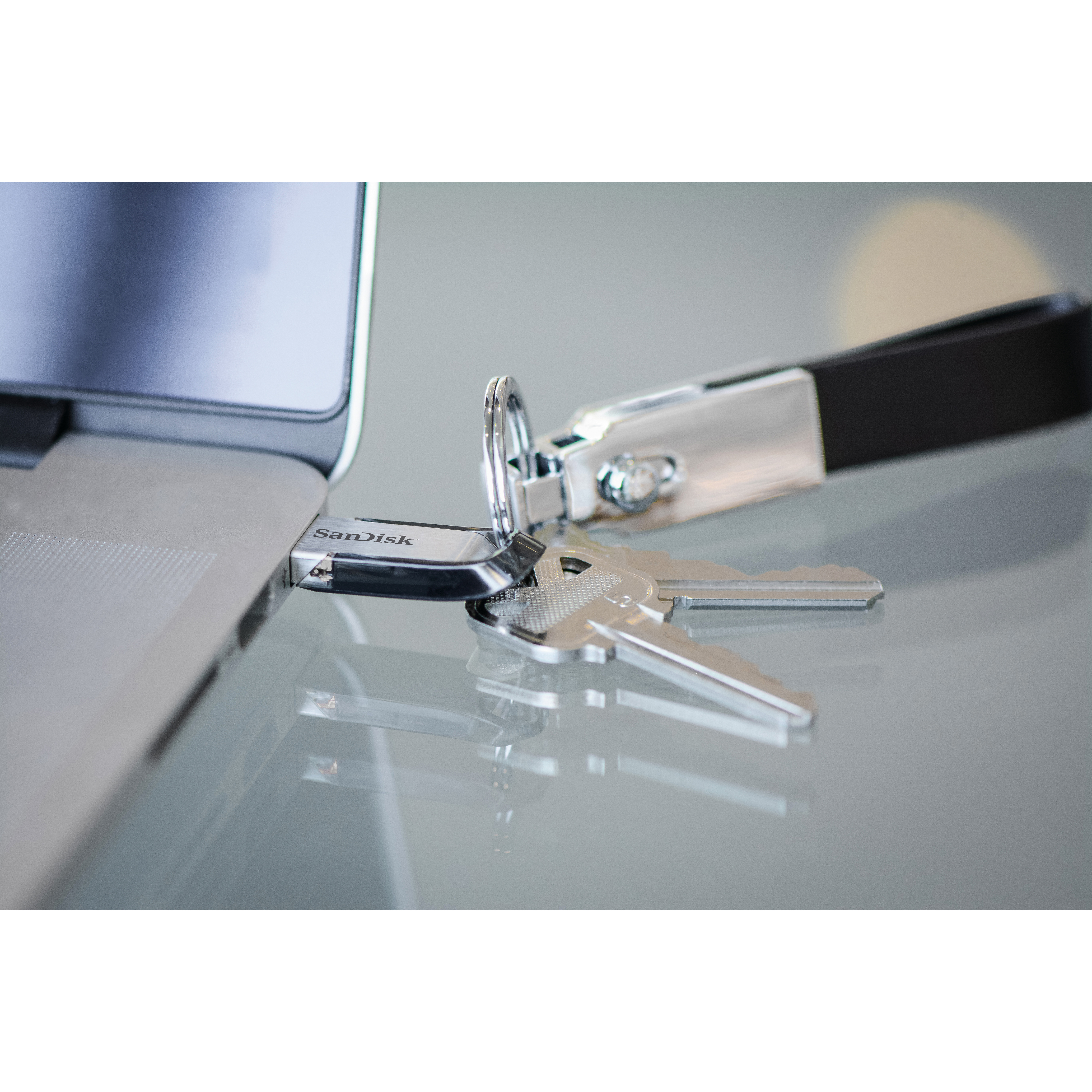 A USB drive and keys are on a laptop. The USB drive says Sandisk.