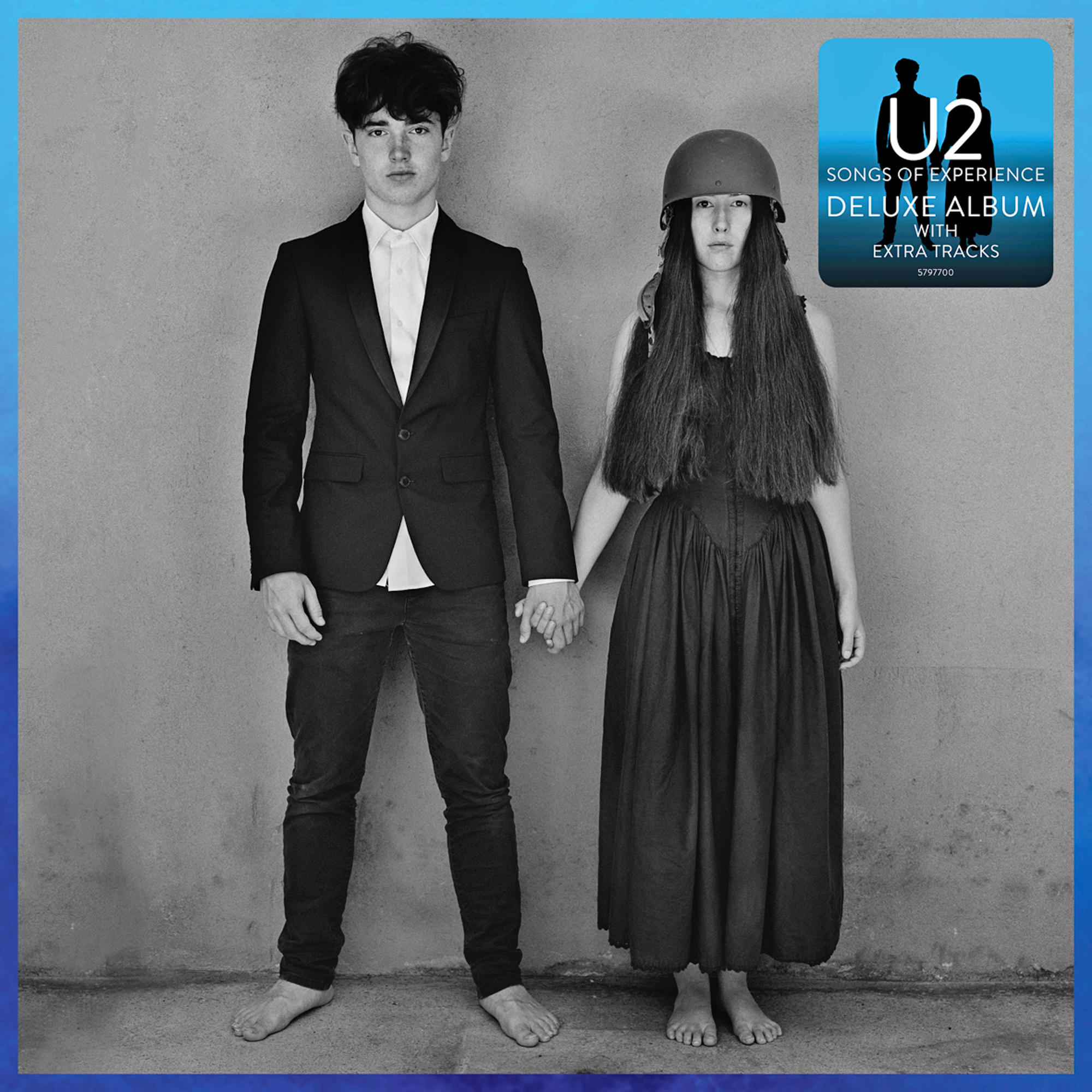 Ein Mann im Anzug und eine Frau im Kleid halten Händchen, vor einer grauen Wand. U2-Albumcover oben rechts.