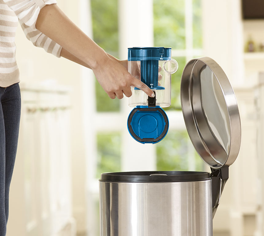 La main d'une femme retire un filtre bleu d'une poubelle argentée, à l'intérieur, avec une cuisine en arrière-plan.