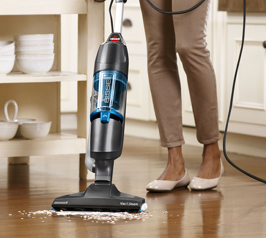 Personne utilisant un aspirateur Bissell noir et bleu sur un plancher en bois.