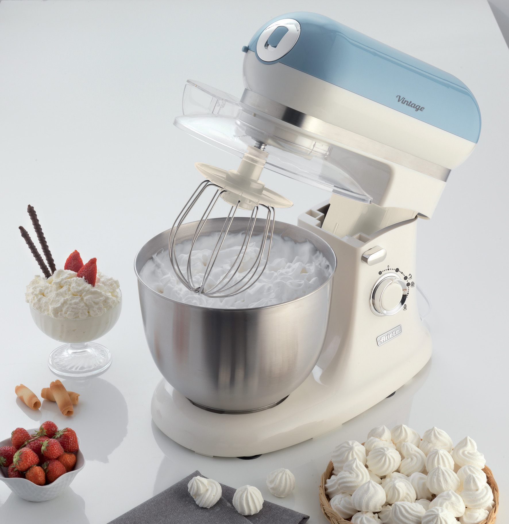 Robot da cucina con una ciotola, meringhe e fragole sul bancone. Colore bianco e blu.