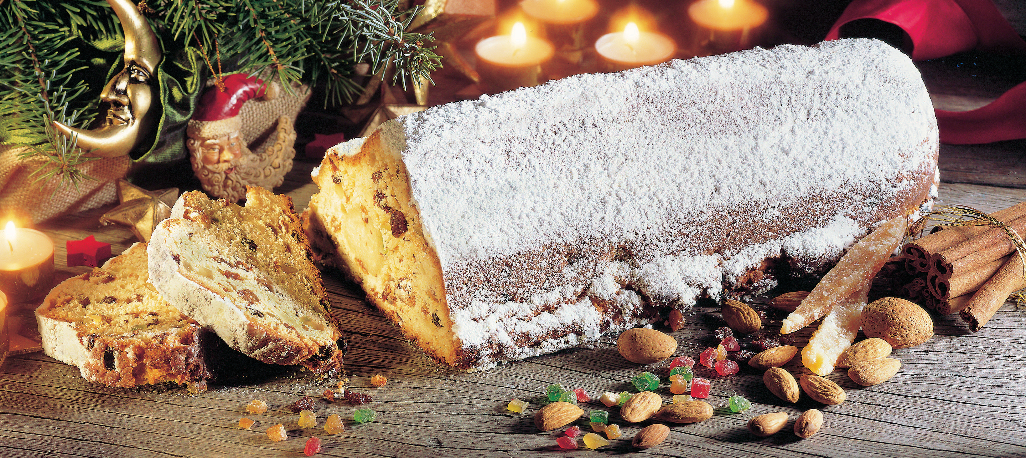 Weihnachtsstollen, angeschnitten, mit Puderzucker bestäubt, mit Mandeln, Zimt und Kerzen.