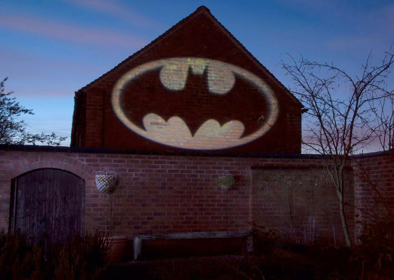 Ein Backsteinhaus mit dem Batman-Logo, das auf es projiziert wird, mit einem bewölkten Himmel.