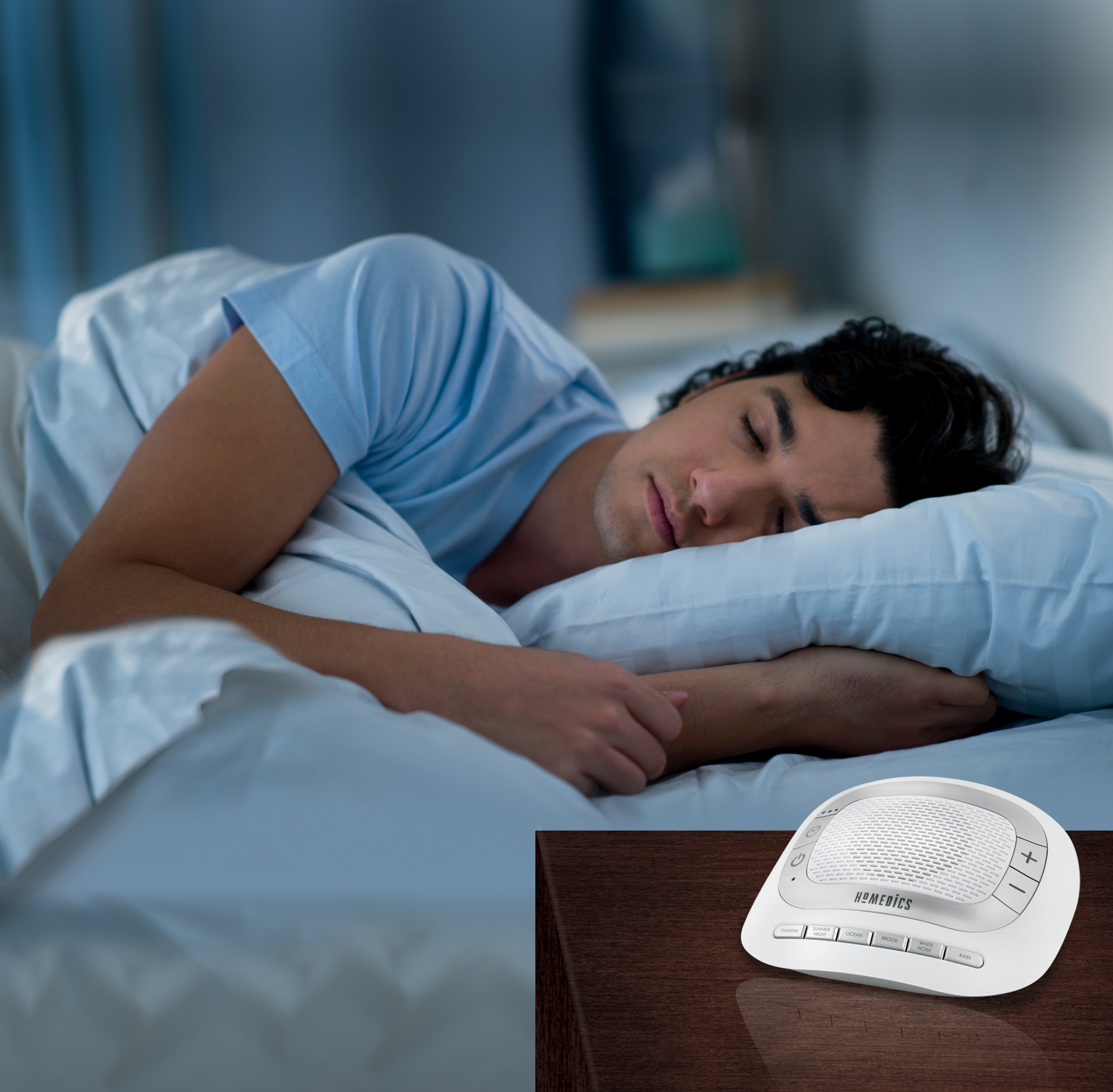 Een man die in bed slaapt met een witte geluidsmachine op een nachtkastje.