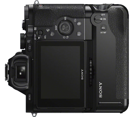Black camera with buttons and display. It is placed on a white surface. Top view.