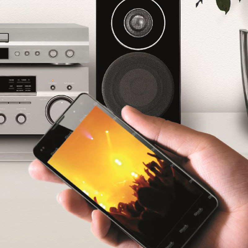 De hand van een persoon die een telefoon vasthoudt met een concert. Luidsprekers en audioapparatuur op de achtergrond.