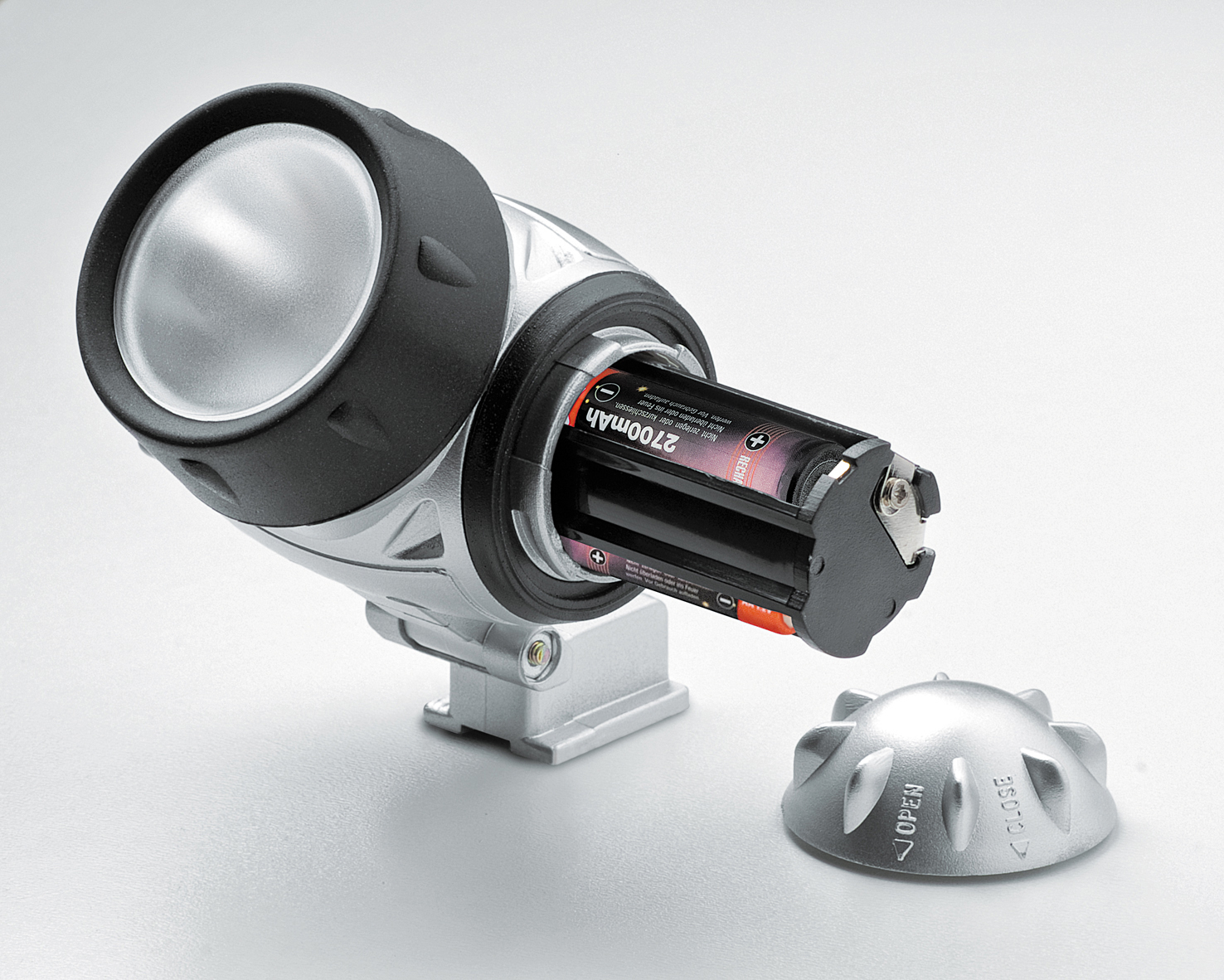 Eine silberne Stirnlampe mit zwei Batterien im Inneren. Der offene Batteriefachdeckel ist im Vordergrund.